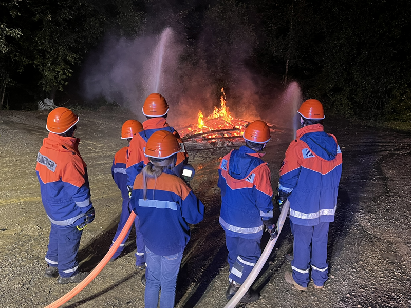 Mehrere Jugendfeuerwehrmitglieder, die mit einem Wasserstrahl ein Feuer löschen. 