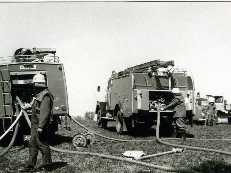 Historische Einsatzfahrzeuge im Löscheinsatz. Bild wird schwarz-weiß dargestellt. 