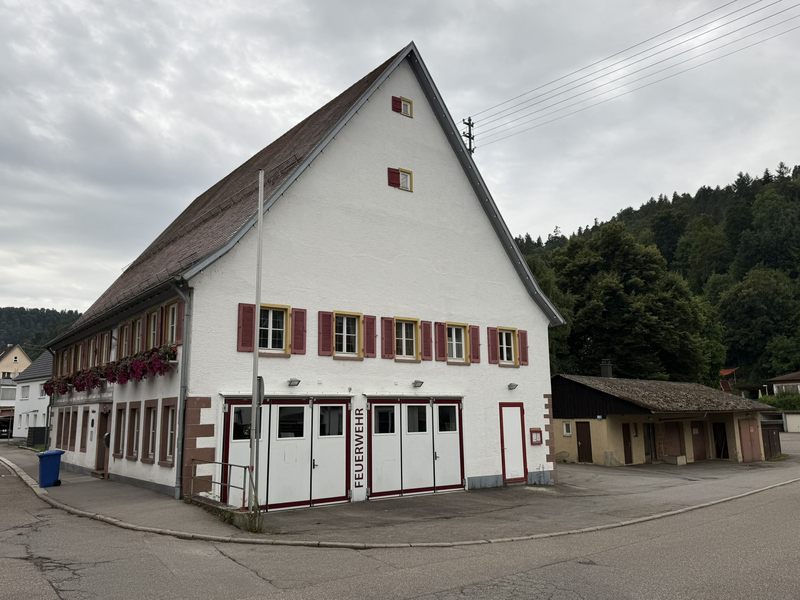 Feuerwehrhaus Aistaig in Seitenansicht. zwei größere Garagentore für die Fahrzeuge sind zu sehen. Darüber 5 Fenster mit Holz-Fensterläden. 