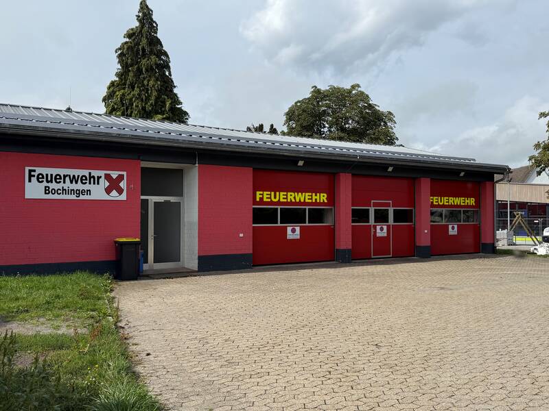 Feuerwehrhaus Bochingen mit drei großen Garagentoren für die Fahrzeugen. Logo der Feuerwehr Bochingen auf der roten Fasade abgebildet. 