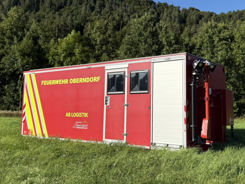 Ein roter Container mit dem Schriftzug AB Logistik steht auf einer Wiese. Der Container hat zwei Fenster und ein Rolltor. 
