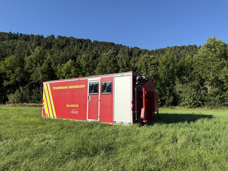 Ein roter Container mit dem Schriftzug AB Logistik steht auf einer Wiese. Der Container hat zwei Fenster und ein Rolltor. 
