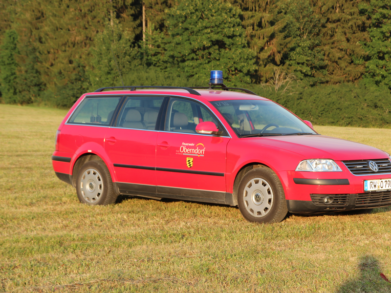 Älterer VW-Kombi steht auf einer Wiese. Eine ältere runde blaue Sirene ist auf dem Dach. An der Seite ist ein älteres Logo der Stadt Oberndorf abgebildet.