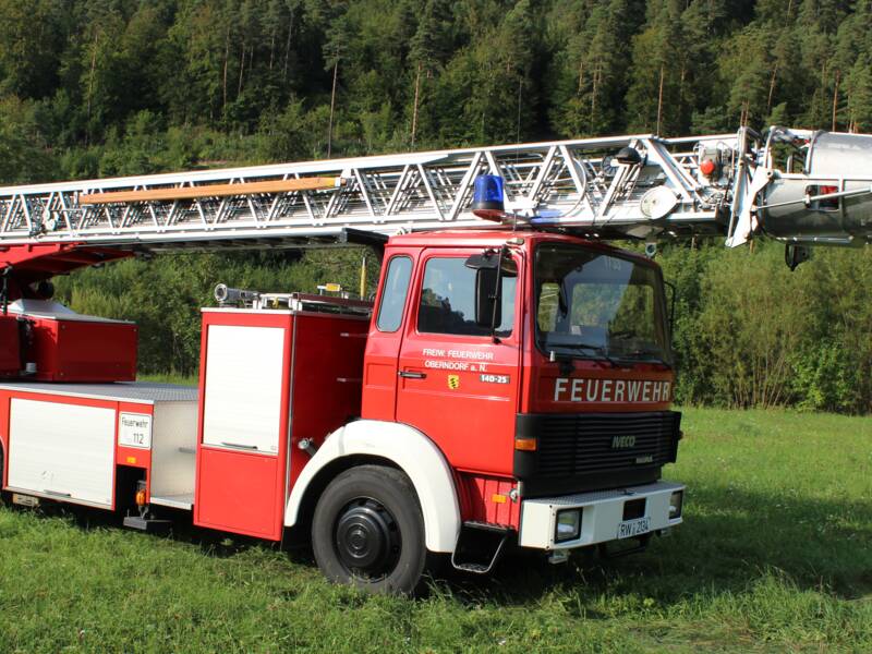 Feuerwehrauto bestehend aus einer großen drehbaren Leiter und einem kleineren Schrank auf der Ladefläche. 