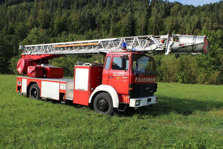 Feuerwehrauto bestehend aus einer großen drehbaren Leiter und einem kleineren Schrank auf der Ladefläche. 