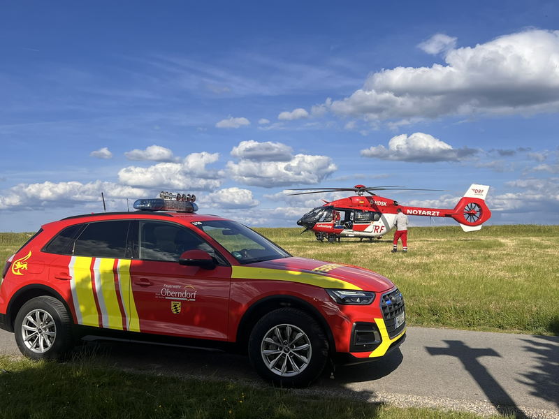 Kommandowagen auf einem Feldweg vor eine gelandeten Rettungshubschrauber. 