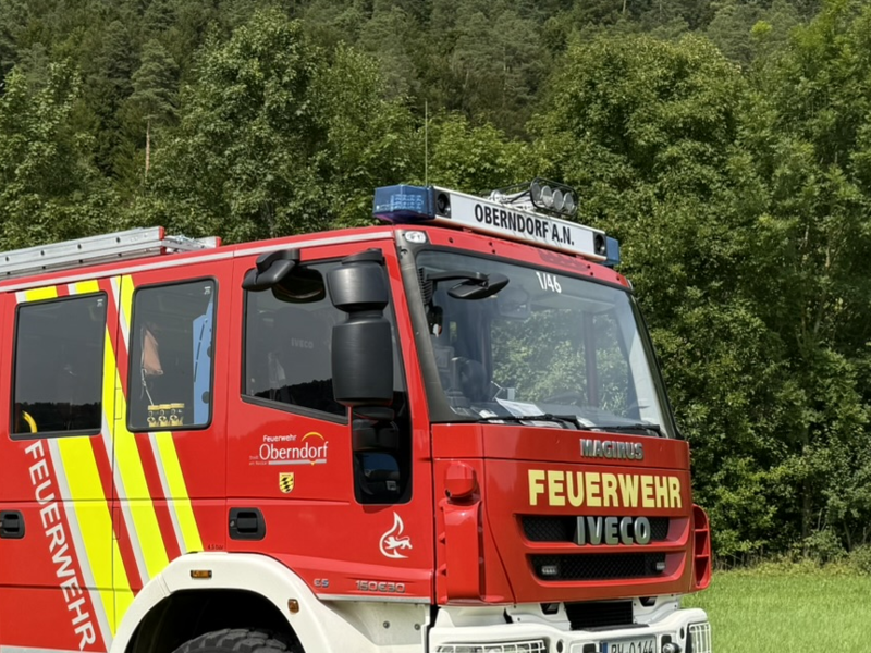 Feuerwehr-Löschfahrzeug steht auf einer Wiese. Seitenansicht mit drei Rolltoren. Schriftzug Feuerwehr Oberndorf a.N. Auf der Frontscheibe steht die Fahrzeugnummer 1/46 