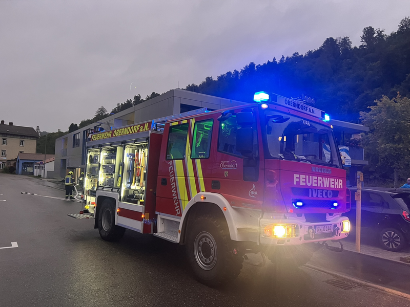 Hilfeleistungslöschfahrzeug in der Dämmerung mit eingeschaltetem Blaulicht vor einem Gebäude.