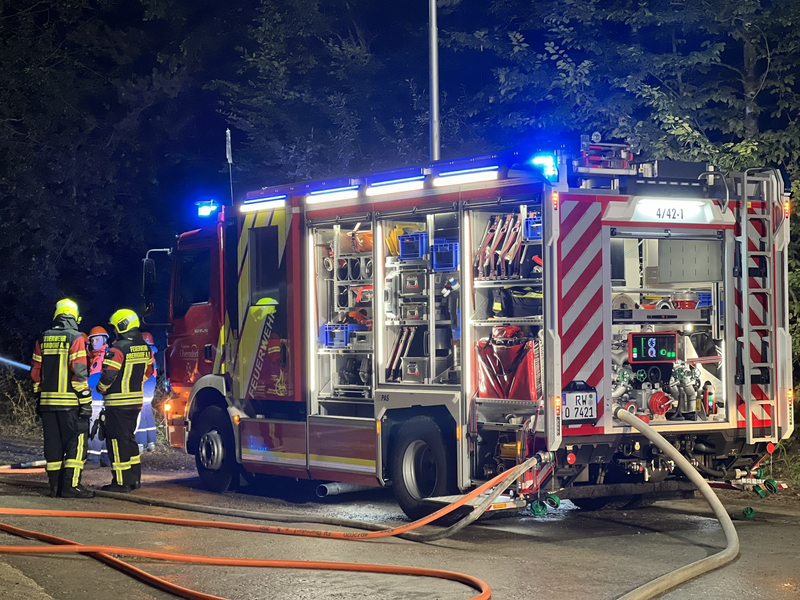 Löschgruppenfahrzeug an einer Einsatzstelle mit angeschlossenen Schläuchen und eingeschaltetem Blaulicht.
