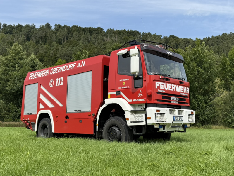 Lösch-Feuerwehrfahrzeug aus Seitenansicht. Steht auf einer Wieser. Farben sind rot/gelb.
