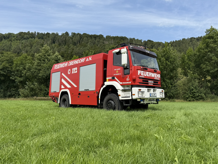 Lösch-Feuerwehrfahrzeug aus Seitenansicht. Steht auf einer Wieser. Farben sind rot/gelb.