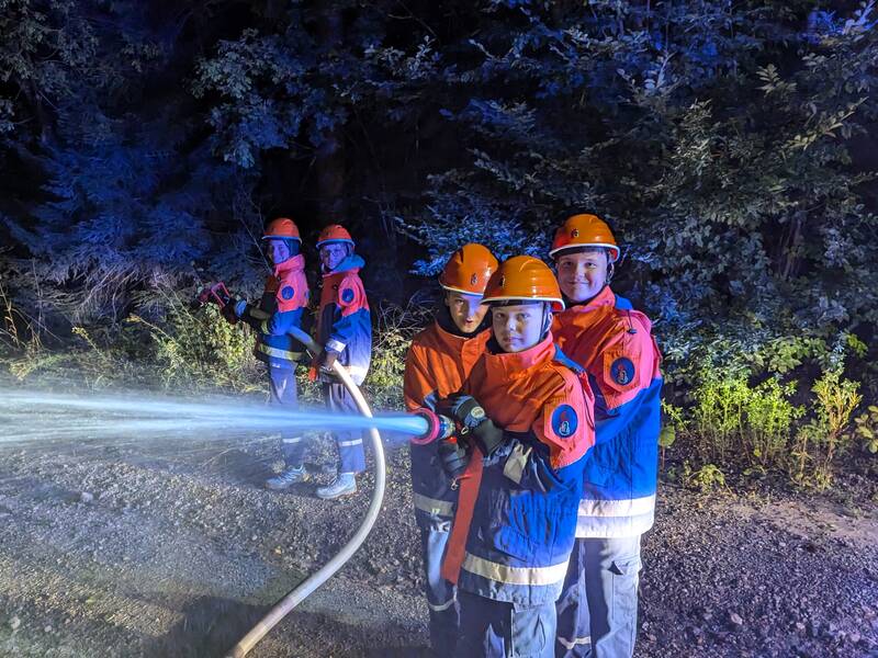 5 Feuerwehr-Kinder halten einen Feuerwehrschlauch und Löschen ein Übungsfeuer.