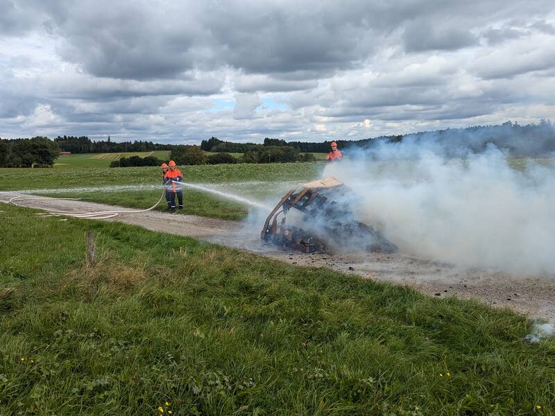 Auf einem Feldweg löschen Feuerwehr-Kinder und -Jugendliche ein brennendes Objekt. 