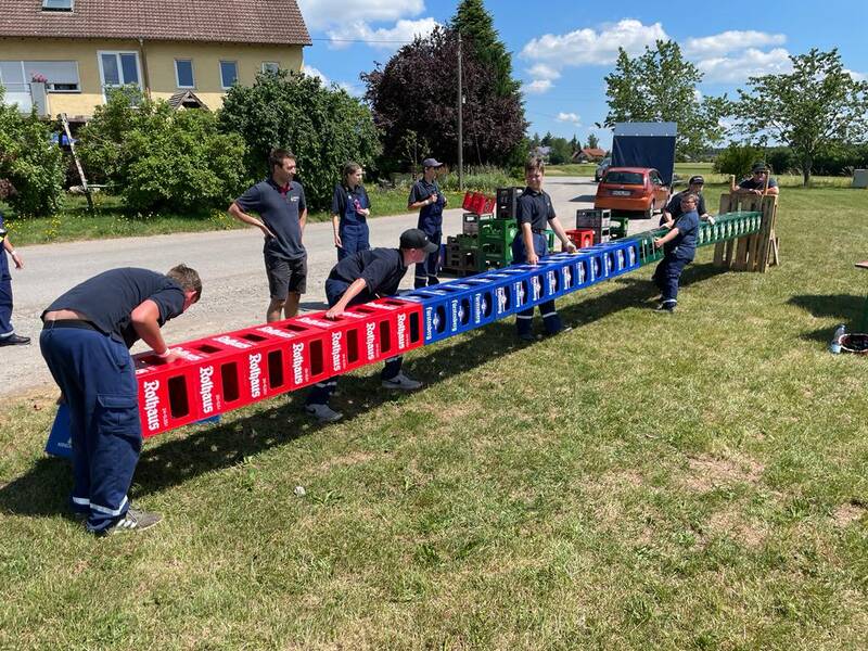 Kinder in Feuerwehrbekleidung versuchen leere Getränkekisten waagerecht in der Luft zu stapeln. 