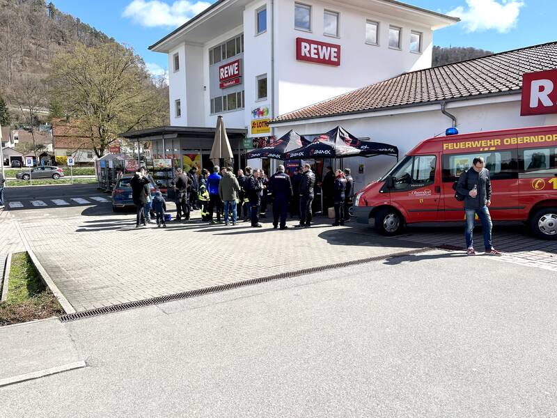 Jugendliche verkaufen vor einem Rewe-Markt Getränke und Würstchen. Viele Besucher stehen um den Stand. 
