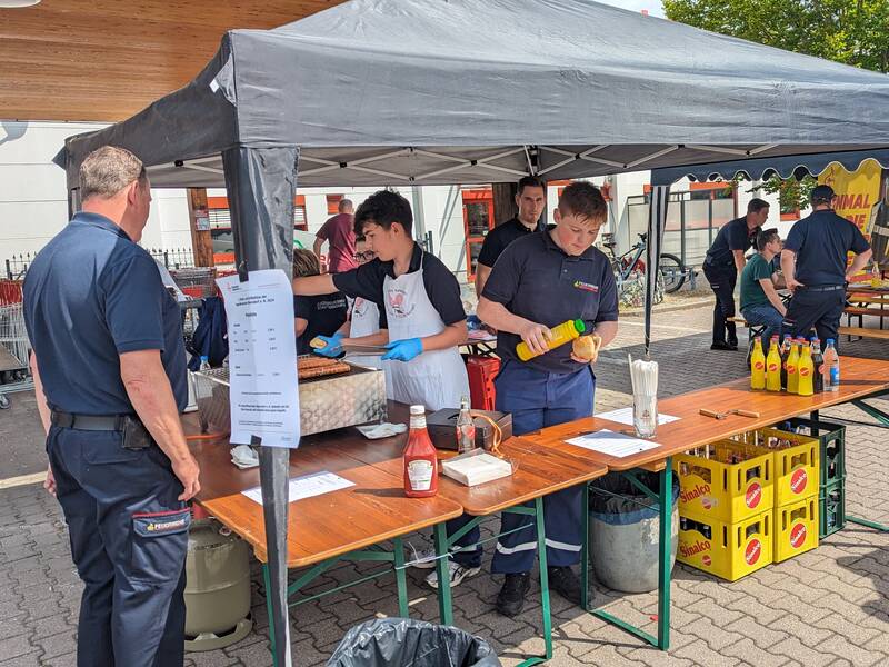 Verkaufsstand mit Zeltüberdachung. Jugendliche grillen und verkaufen Würstchen und Getränke.