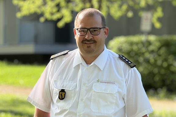Männliche Person mit kurzen Haaren und Brille. Weißes Feuerwehrhemd mit schwarzer Hose. 
