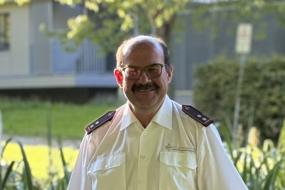 Eine männliche Person mit Brille steht auf einer Brücke und lächelt in die Kamera. Er hat ein weißes Feuerwehrhemd und schwarze Hose an. 